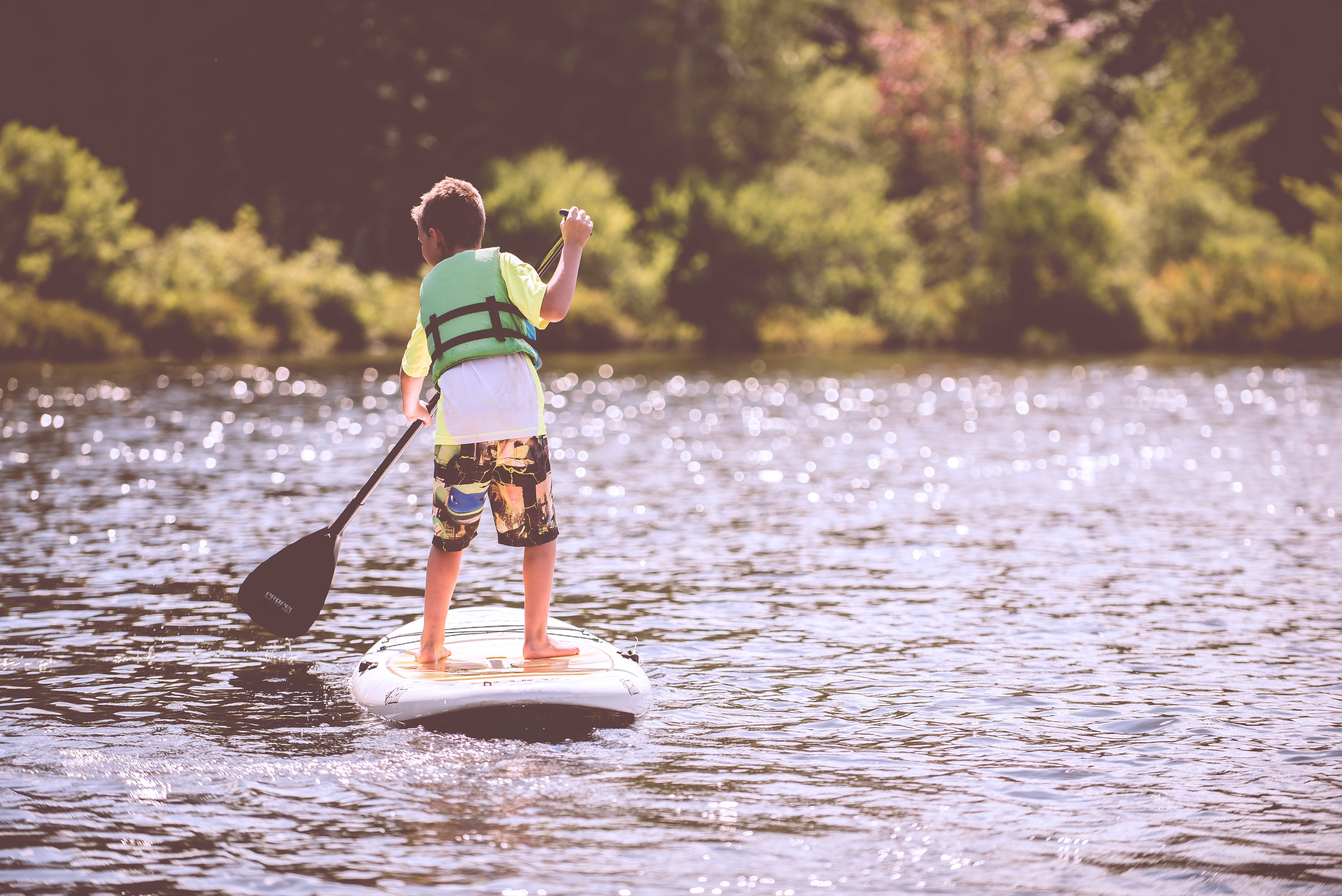 Young boy wearing life jacket and standing on paddleboard in a lake
