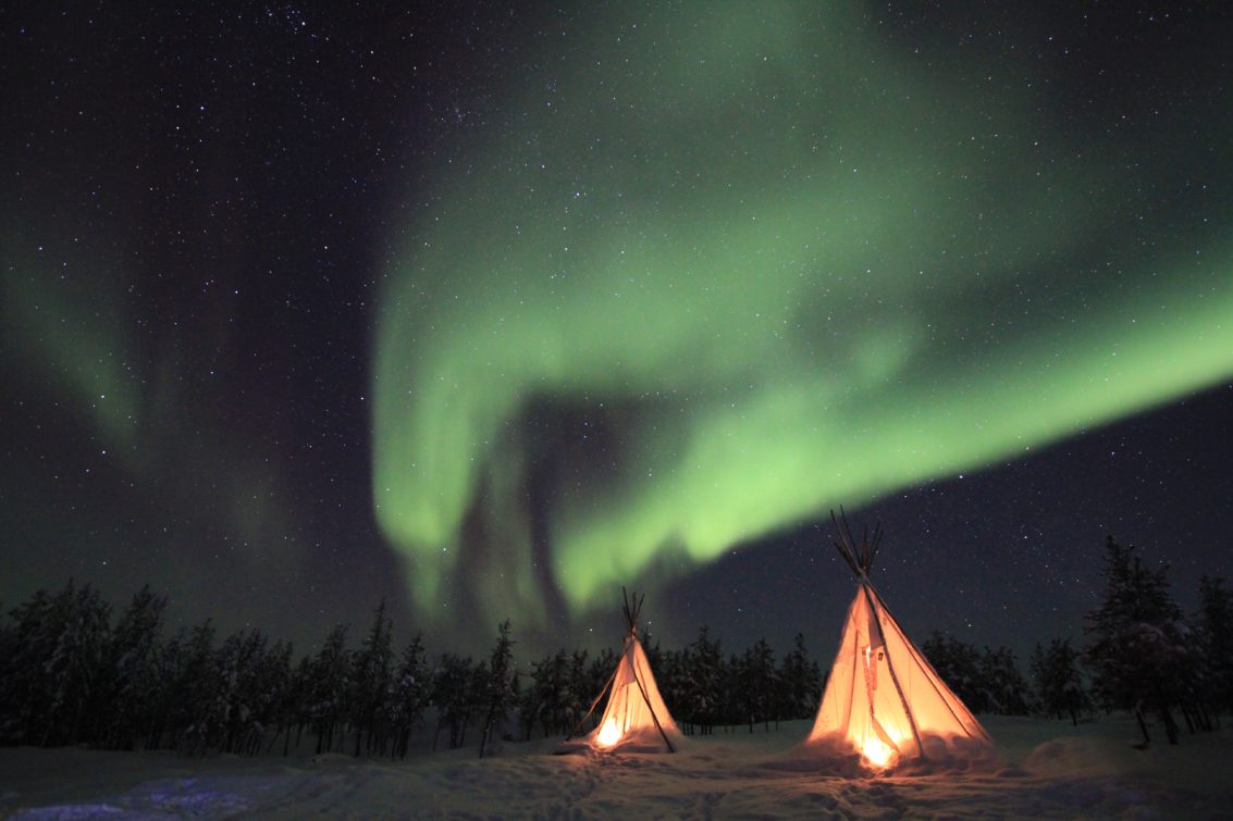two tipi's in winter forest under northern lights