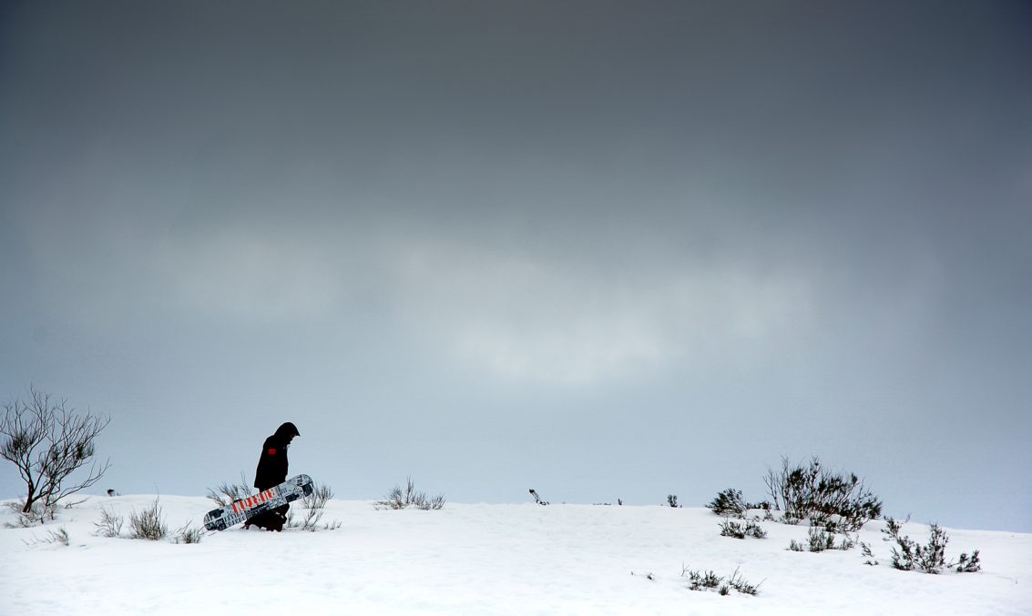 man walking through snow with snowboard