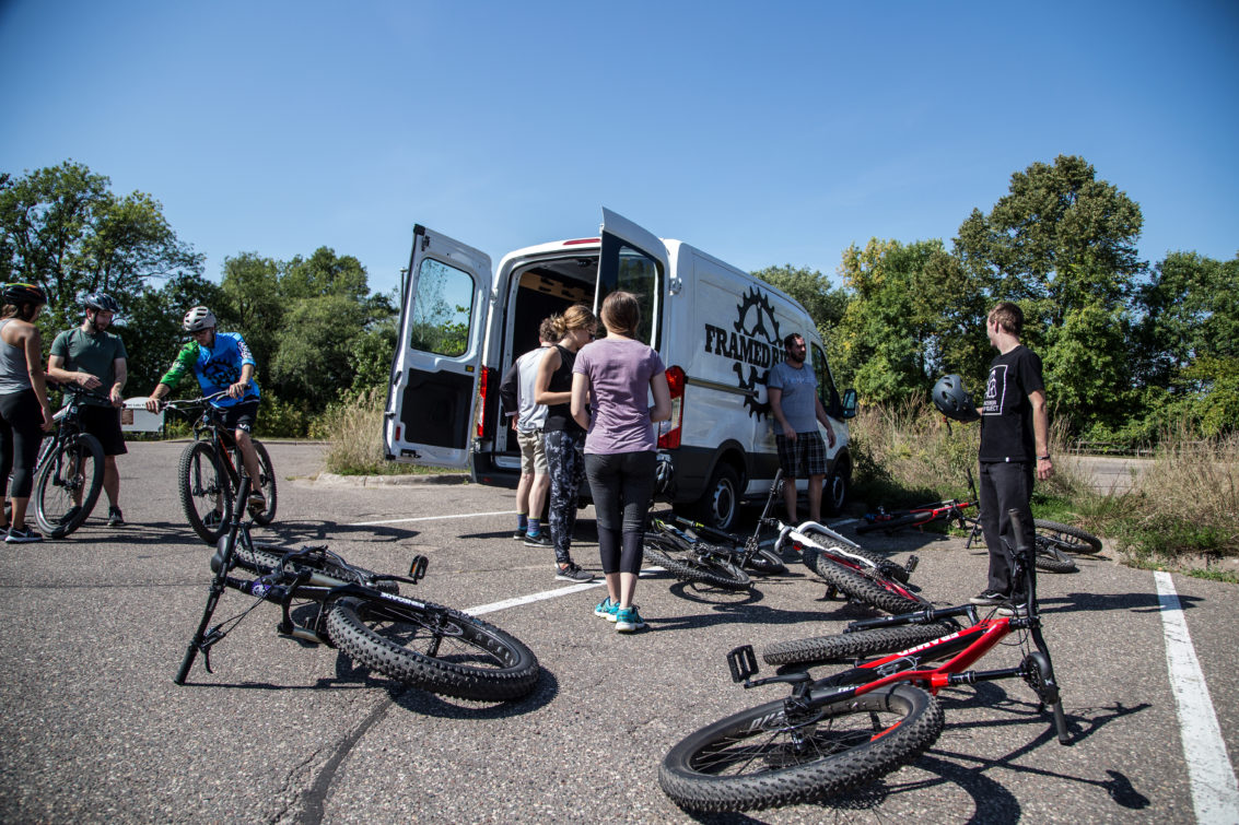 mountain bikers standing in a parking lot next to a van
